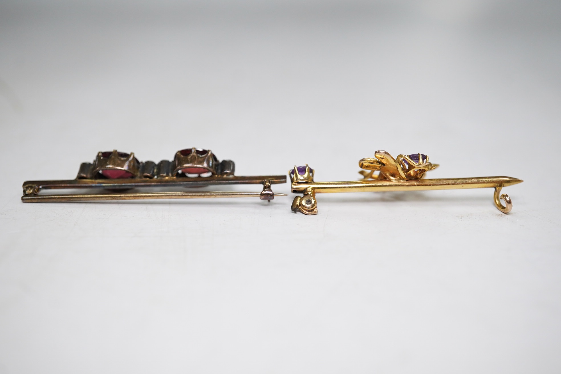 An Edwardian 375, amethyst and seed pearl set bug bar brooch, 39mm (lacking pin) and a yellow metal, garnet? and diamond chip set bar brooch, gross weight 4.4 grams. Condition - poor to fair